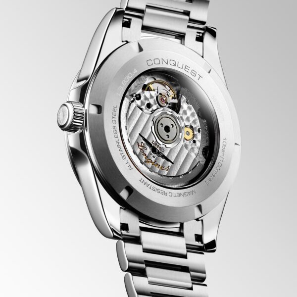 Die Longines Conquest 2023 ist eine silberne Armbanduhr mit filigranen Zahnrädern, die durch eine transparente Rückseite sichtbar sind. „Conquest“ und weitere Details sind in das Metall rund um das Glas eingraviert. Das Armband ist silberfarben und die Aufzugskrone ist markant.