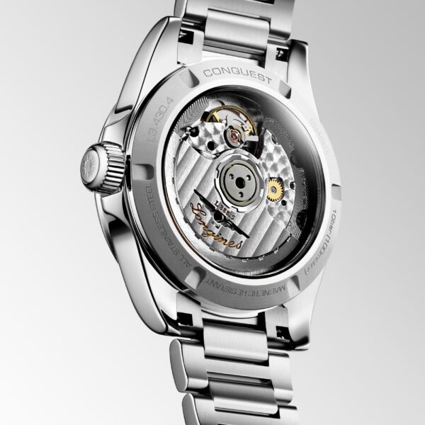 Die Rückseite der Longines Conquest 2023 gibt durch einen transparenten Gehäuseboden den Blick auf ihr komplexes mechanisches Uhrwerk frei. Diese luxuriöse Armbanduhr aus silbernem Metall besticht durch ein poliertes Gliederarmband und gravierte Details, die die inneren Zahnräder und Komponenten sichtbar machen.