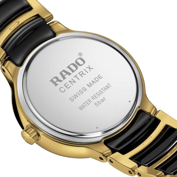 Nahaufnahme der Rückseite einer Rado Centrix Diamonds. Die polierte Metalloberfläche ist mit den Gravuren „RADO CENTRIX“, „SWISS MADE“ und „WATER RESISTANT 5 bar“ versehen. Die Uhr verfügt über ein gold-schwarzes Gliederarmband.