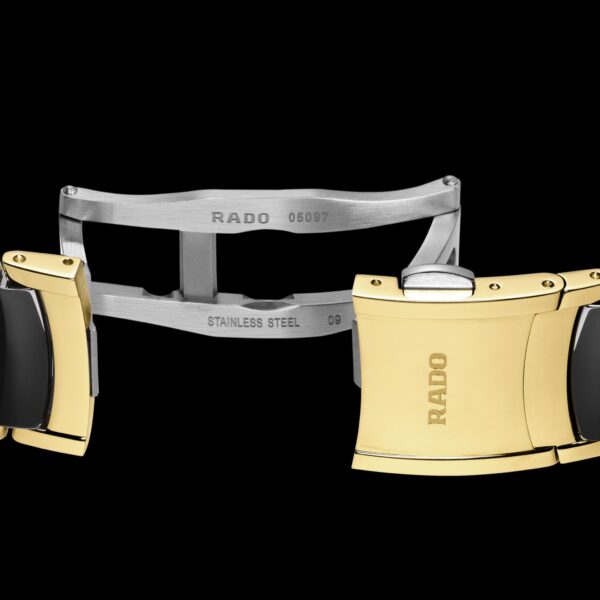 Nahaufnahme eines Rado Centrix Automatic Diamonds-Uhrenarmbands mit goldenen und schwarzen Gliedern und einer Edelstahlschließe. Sowohl auf dem Endglied als auch auf der Schließe ist „Rado“ eingraviert, außerdem stehen dort „STAINLESS STEEL“ und „05057“.