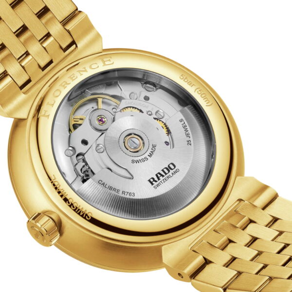Eine Nahaufnahme der Rado Florence Automatic zeigt eine goldene Armbanduhr mit Schweizer Uhrwerk. Die Rückseite trägt den Schriftzug „Florence“ und Details zur Wasserdichtigkeit, während das goldene Armband ein gewebtes Design aufweist.