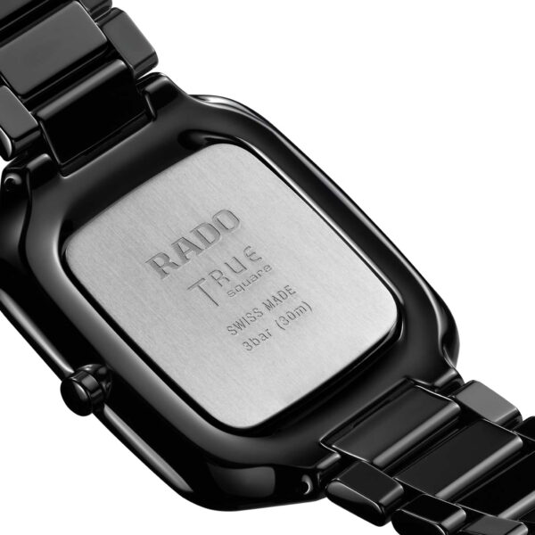 Nahaufnahme der Rückseite einer Rado True Square Thinline Armbanduhr. Das quadratische Gehäuse mit abgerundeten Kanten ist aus Metall und trägt die Aufschrift „RADO TRUE Thinline SWISS MADE 3 bar (30 m)“. Ein glänzend schwarzes Keramikarmband mit glänzender Oberfläche rundet das Modell ab.