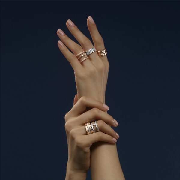 Zwei elegant positionierte Hände, geschmückt mit Chopard Ice Cube Ringen in Gold und Silber, vor dunklem Hintergrund. Anmutig ineinander verschlungene Finger betonen das filigrane Design jedes Rings.
