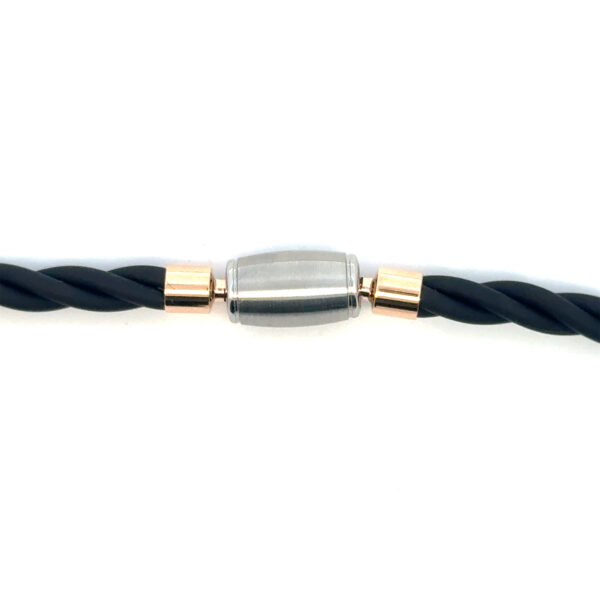 Eine Nahaufnahme zeigt das Jörg Heinz Tönnchen matt: ein schwarzes, gedrehtes Kabel mit einem metallischen, zylindrischen Stecker, silberfarben mit goldenen Akzenten an jedem Ende, vor einem weißen Hintergrund.