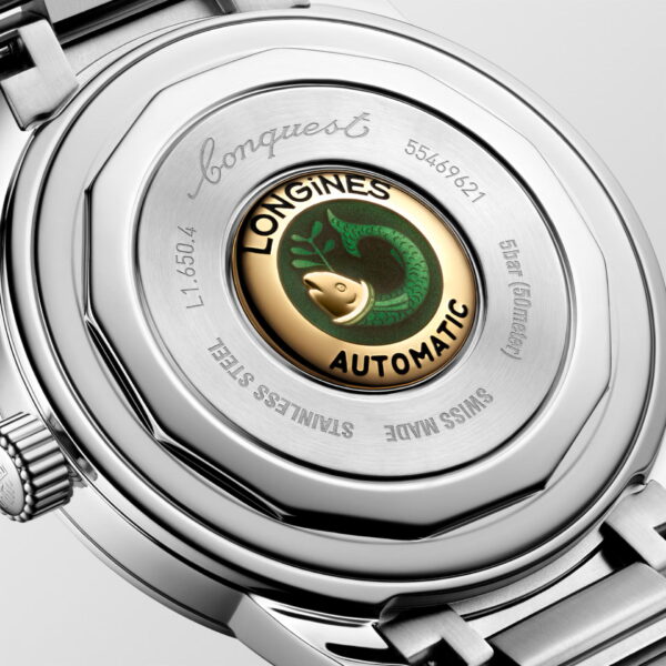 Nahaufnahme der Rückseite einer Longines Conquest Heritage mit einem gold-grünen Fischemblem und eingraviertem Text mit Modell- und Materialdetails auf dem Edelstahlgehäuse.