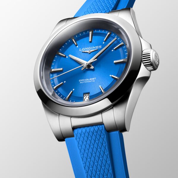 Die Longines Conquest Uhr verfügt über ein silbernes Gehäuse, ein hellblaues Zifferblatt mit silbernen Indexen und ein passendes, strukturiertes blaues Armband auf einem hellgrauen Hintergrund.