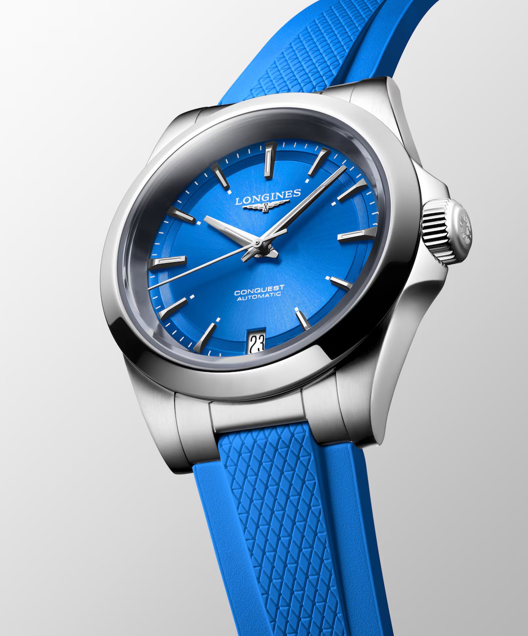 Die Longines Conquest Uhr verfügt über ein silbernes Gehäuse, ein hellblaues Zifferblatt mit silbernen Indexen und ein passendes, strukturiertes blaues Armband auf einem hellgrauen Hintergrund.