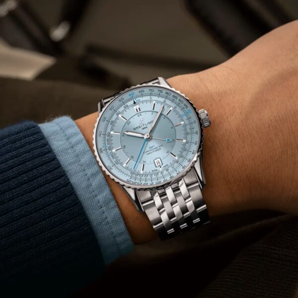 Eine Person trägt eine silberne Breitling Navitimer Automatic GMT 41 mit hellblauem Zifferblatt, Datumsfenster und Metallgliederband. Ihr Ärmel ist blau und der Hintergrund ist unscharf.