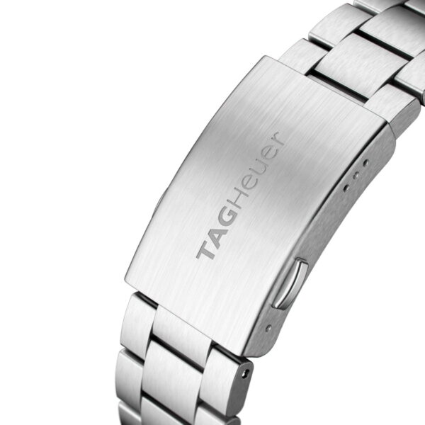 Nahaufnahme eines silbernen Tag Heuer Formula 1-Metallarmbands und -Verschlusses mit dem eingravierten Logo auf einer gebürsteten Oberfläche mit polierten und gebürsteten Gliedern.
