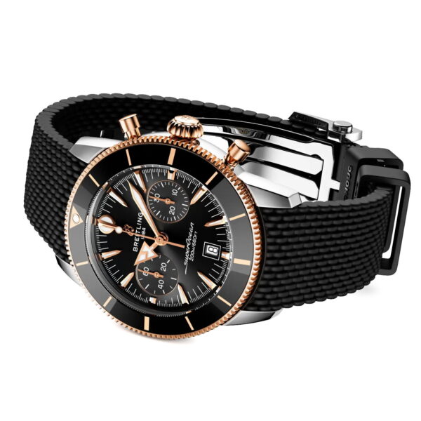 Die Breitling Superocean Heritage B01 Chronograph 42 verfügt über ein schwarzes strukturiertes Armband, ein schwarzes Zifferblatt, eine Lünette aus Roségold und Drücker aus Roségold, die schräg auf einem weißen Hintergrund abgebildet sind.