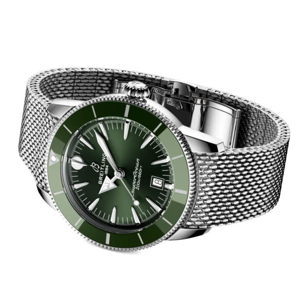 Eine Breitling Superocean Heritage B31 Automatic 44 Armbanduhr mit grünem Zifferblatt und Lünette, silbernem Netzarmband, silbernen Stundenmarkierungen und Datumsfenster bei 3 Uhr, schräg auf weißem Hintergrund.