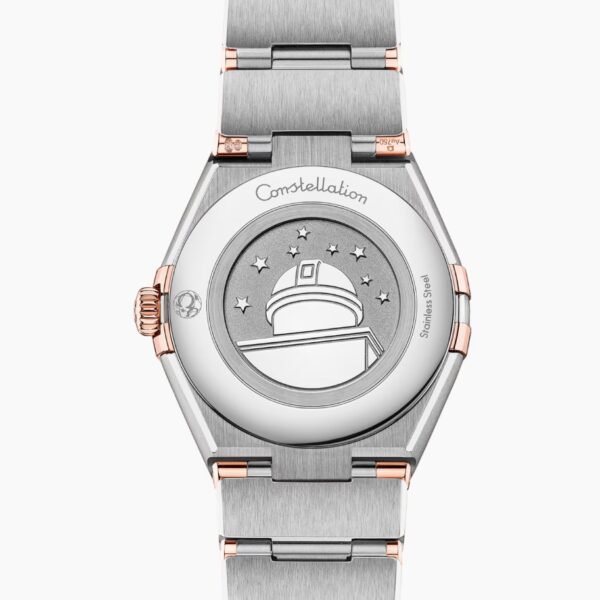 Eine Nahaufnahme des Gehäusebodens der OMEGA Constellation Manhattan aus Silber und Roségold zeigt eine gravierte Sternwartenkuppel mit Sternen und dem Wort "Constellation" über dem Design.