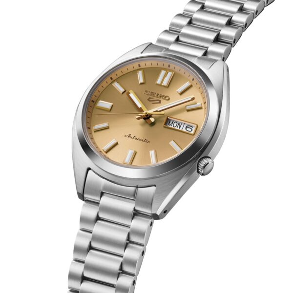 Eine SNX SEIKO 5 Automatik Armbanduhr mit silbernem Gehäuse, goldenem Zifferblatt, silbernen Stundenmarkierungen und Zeigern, Tages-/Datumsanzeige und einem Edelstahlgliederarmband. Auf dem Zifferblatt steht "Automatic.