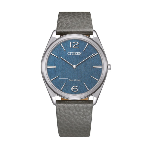Die Citizen Eco-Drive Suratto verfügt über ein blaues, strukturiertes Zifferblatt, silberne Indexe und Zeiger, ein silbernes Gehäuse, ein graues Lederarmband, markante 12- und 6-Ziffern und das "CITIZEN"-Logo an der Spitze.
