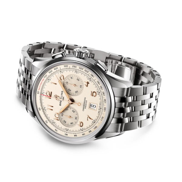 Ein Breitling Premier B01 Chronograph aus Edelstahl mit einem cremefarbenen Zifferblatt, silbernen Zeigern und Indizes, drei Hilfszifferblättern und einem Metallgliederarmband, das schräg auf einem weißen Hintergrund angebracht ist.