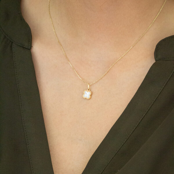 Eine Person, die eine olivgrüne Bluse und eine zarte Goldkette mit einem kleinen, blumenförmigen Anhänger trägt.