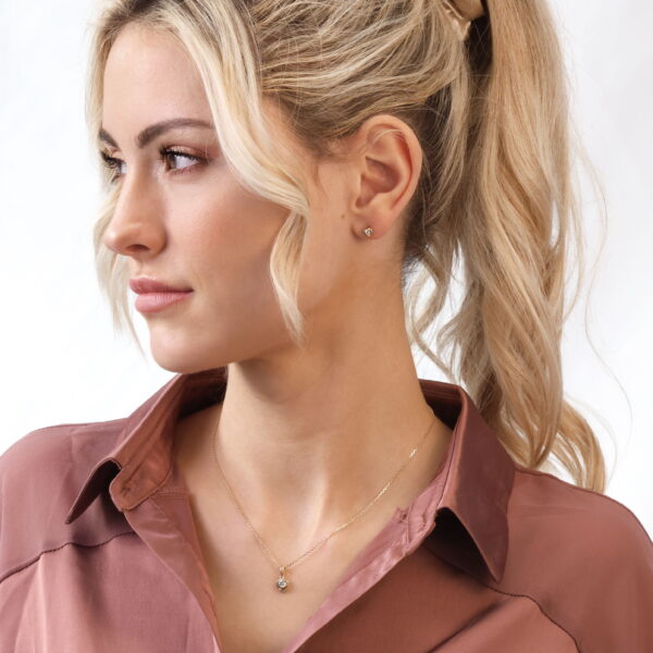 Eine Frau mit langem, gewelltem blondem Haar in einem Pferdeschwanz und kleinen Ohrsteckern trägt die Echtgold Collier Rosamée Halskette und eine mauvefarbene Satinbluse und blickt zur Seite vor einem schlichten Hintergrund.