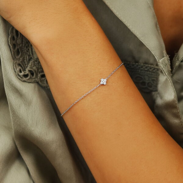 Nahaufnahme einer Person, die das Delicate Touch Armband Clover Silber, ein zartes Silberarmband, an ihrem Handgelenk trägt, gekleidet in salbeigrünen Stoff mit Spitzendetails.