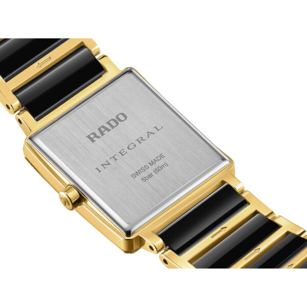 Nahaufnahme der Rückseite einer Rado Integral Diamonds Uhr mit einem rechteckigen silbernen Gehäuse, auf dem "RADO INTEGRAL SWISS MADE 5 bar (50m)" eingraviert ist und das an einem goldenen und schwarzen Keramik-Gliederarmband befestigt ist.