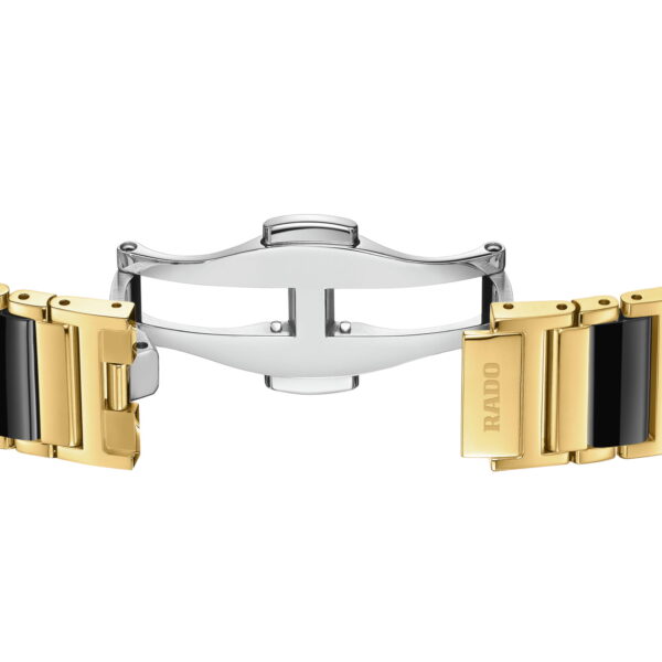 Eine Nahaufnahme des Rado Integral Diamonds Armbands mit goldenen, schwarzen und silbernen Gliedern und einer offenen Faltschließe aus Edelstahl mit eingraviertem Rado-Logo.