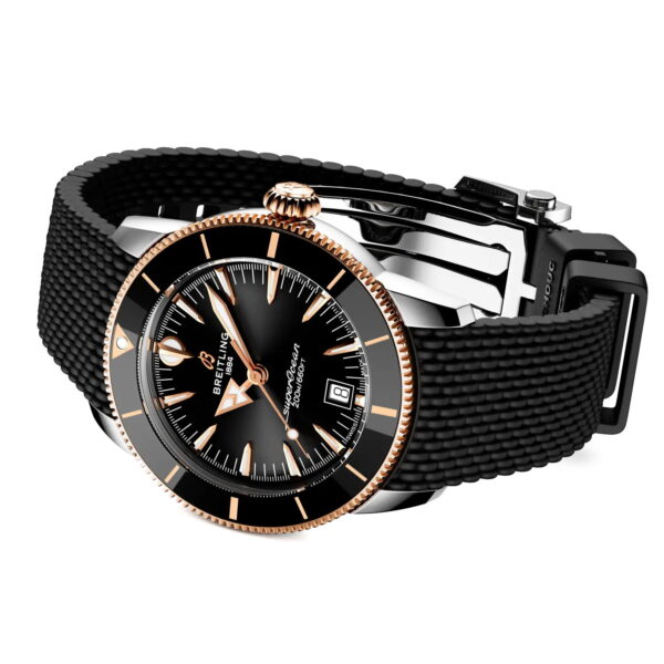 Die Breitling Superocean Heritage B31 Automatic 42 verfügt über ein schwarzes, strukturiertes Armband, ein schwarzes Zifferblatt mit goldenen Akzenten und eine Datumsanzeige, die schräg auf einem weißen Hintergrund angebracht ist.