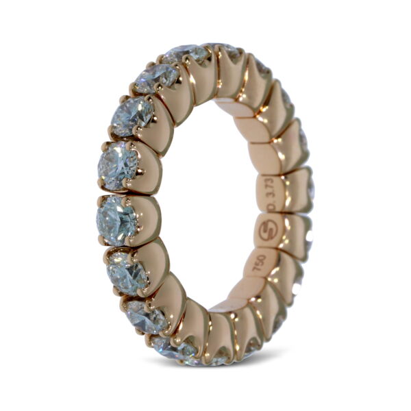 Der Scheffel Stretch Coronet Damenring ist ein goldener Ewigkeitsring mit runden, klaren Edelsteinen, die um das Band herum gefasst sind, auf einem weißen Hintergrund.