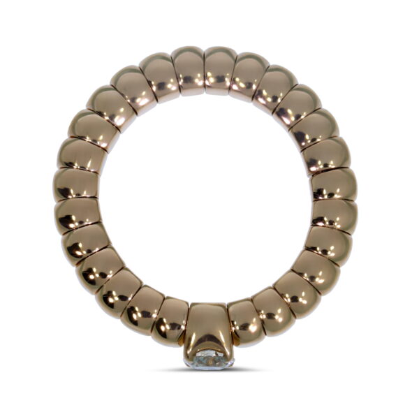 Der Scheffel Stretch Ring Solitair besteht aus einem goldenen, segmentierten Band mit einem abgerundeten, perlenförmigen Design und einem einzelnen klaren Edelstein am unteren Ende, der auf weißem Hintergrund zu sehen ist.