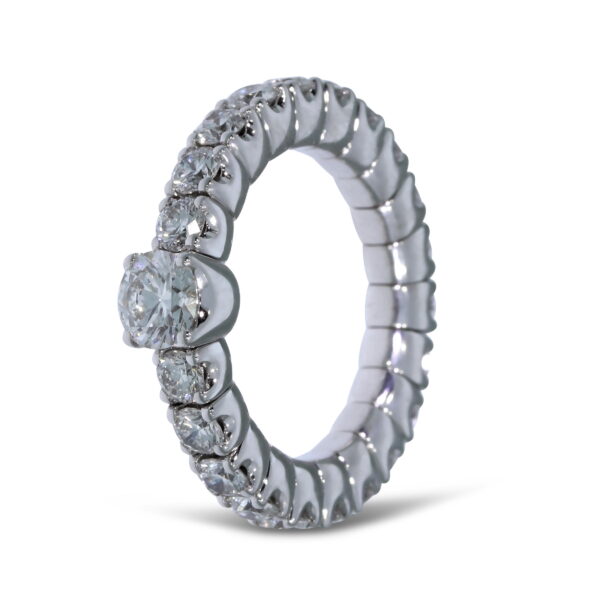 Der Scheffel Stretch Solitaire Damenring ist ein silberner Ewigkeitsring mit Diamanten im Rundschliff und einem größeren Diamanten in der Mitte, der vor einem weißen Hintergrund gezeigt wird.