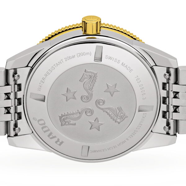 Die Rückseite der Rado Captain Cook Automatic zeigt ein silbernes Metallarmband, eine goldene Krone und eingravierte Seepferdchen und Sterne sowie Markendetails wie "Swiss Made", Wasserdichtigkeit und Spezifikationen aus Edelstahl.