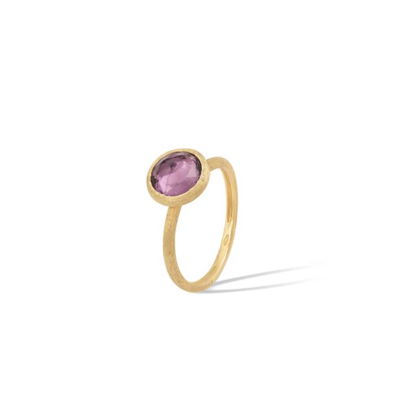 Ein Goldring mit dünnem Band ist mit einem runden, facettierten violetten Edelstein in einer einfachen Zargenfassung besetzt. Der Ring ist vor einem weißen Hintergrund mit einem Schatten auf der rechten Seite fotografiert.