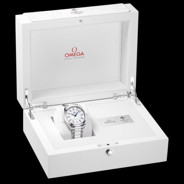 Die OMEGA Seamaster Aqua Terra, eine silberne Armbanduhr mit weißem Zifferblatt und blauen Akzenten, wird in einer offenen weißen Schachtel präsentiert, auf deren Deckel das Omega-Logo und der Text des offiziellen Zeitnehmers zu lesen sind. Eine Karte und ein Booklet sind ebenfalls enthalten.