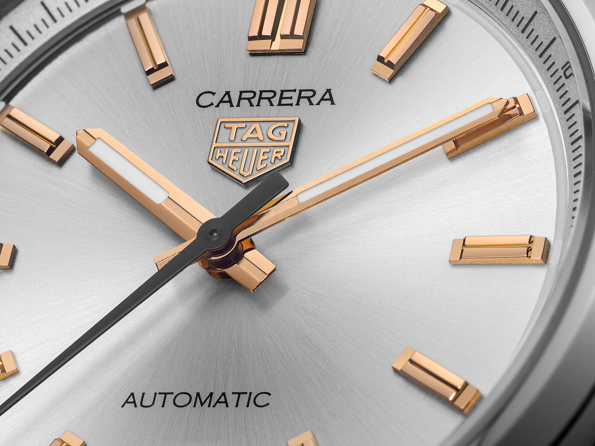 Nahaufnahme des Ziffernblatts einer TAG Heuer Carrera Date mit goldenen Indexen und Zeigern, silberner Sonnenschliffstruktur und schwarzem Text mit dem TAG Heuer-Logo, dem Markennamen und dem Hinweis "Automatic".