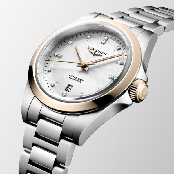 Die Longines Conquest ist eine luxuriöse Armbanduhr aus Edelstahl mit roségoldener Lünette, weißem Zifferblatt, diamantbesetzten Indexen, Datumsfenster bei 6 Uhr und einem Gliederarmband aus Metall, abgebildet auf einem hellen Hintergrund.