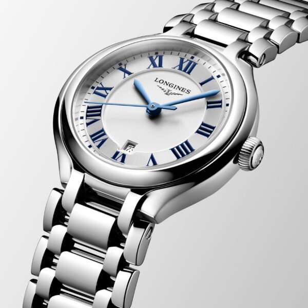 Die Longines Primaluna ist eine silberne Armbanduhr mit einem runden weißen Zifferblatt mit blauen römischen Ziffern, blauen Zeigern, einem Datumsfenster bei 3 Uhr und einem polierten Metallgliederarmband auf hellgrauem Hintergrund.