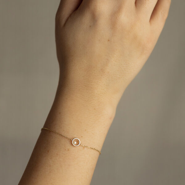 Nahaufnahme einer hellhäutigen Hand, die das Echtgold Armband Champagne trägt, ein zartes Goldarmband mit einem kleinen runden Anhänger vor einem neutralen Hintergrund.