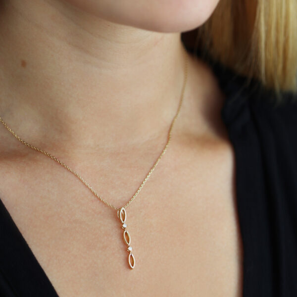 Eine Frau, die von den Schultern aufwärts gezeigt wird, trägt ein schwarzes Oberteil und das Echtgold Collier relier - eine zarte Goldkette mit einem vertikalen Anhänger mit drei kleinen Schleifen.