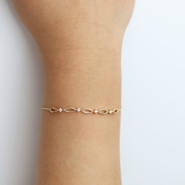 Das Echtgold Armband relier, ein zartes Goldarmband mit kleinen rosa Edelsteinen, wird an einem Handgelenk vor einem schlichten weißen Hintergrund präsentiert.