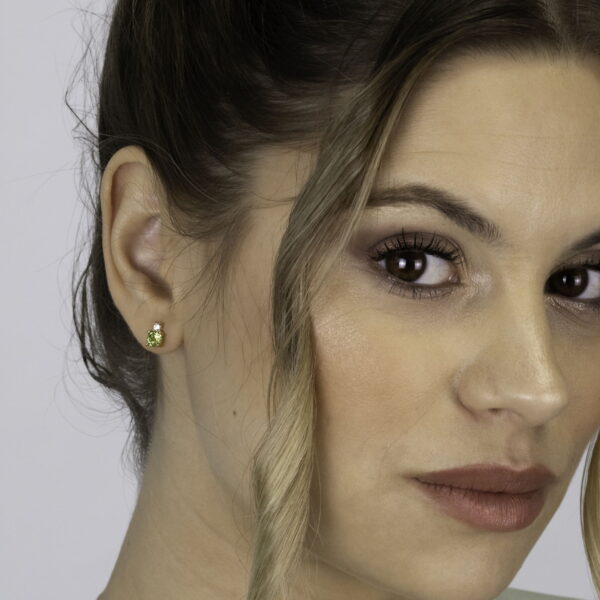 Eine Frau mit hellbraunem Haar in einer Hochsteckfrisur, sanftem Make-up und einem hellen Oberteil trägt Echtgold Ohrringe Douce - kleine goldene Ohrstecker - vor einem schlichten, hellen Hintergrund, ihr Ausdruck ist neutral, während lose Strähnen ihr Gesicht umrahmen.
