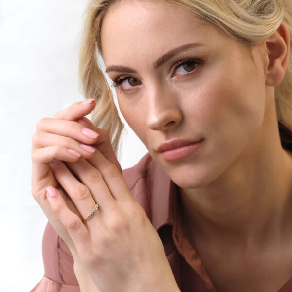 Eine Frau mit blondem Haar und heller Haut, in einem lilafarbenen Kragenhemd, blickt neutral in die Kamera, während sie sanft ihr Gesicht berührt. Sie trägt natürliches Make-up und den zarten Echtgold-Ring Zélina.