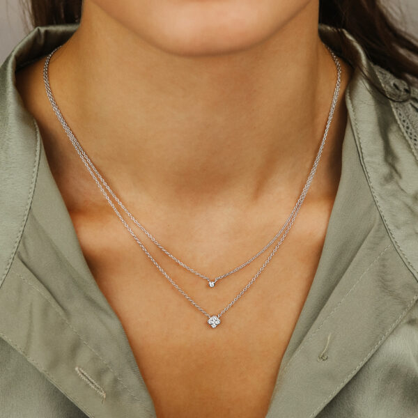 Eine Frau trägt eine hellgrüne Bluse mit V-Ausschnitt und zwei Delicate Touch Collier Clover Silberhalsketten - eine mit einem kleinen Anhänger, die andere mit einem größeren runden Anhänger.
