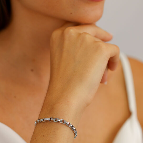 Eine Frau in einem weißen Oberteil lächelt sanft und leicht geschminkt und posiert mit der Hand am Kinn, um das Solid Flair Armband zu zeigen - ein elegantes Silberarmband an ihrem Handgelenk.