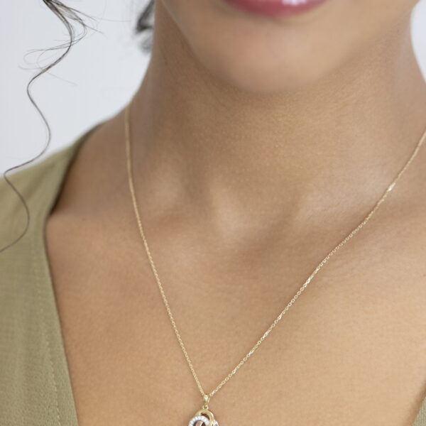 Eine Frau trägt das Echtgold Collier Noyer, eine zarte goldene Halskette mit einem kleinen Knotenanhänger, zu einem hellgrünen Oberteil mit V-Ausschnitt. Der Fokus liegt auf ihrem Hals und ihrem Schmuck; ihre Lippen und ein Teil ihres Gesichts sind zu sehen.
