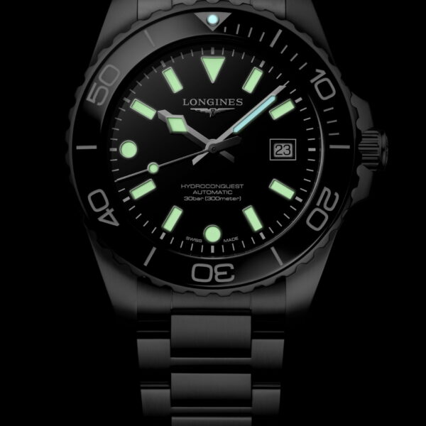 Die Longines HydroConquest verfügt über ein dunkles Metallarmband, ein schwarzes Zifferblatt, grün leuchtende Indexe und Zeiger sowie eine Datumsanzeige bei 3 Uhr.