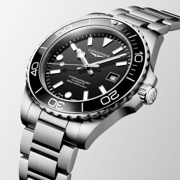 Eine Nahaufnahme der Longines HydroConquest Armbanduhr zeigt das Edelstahlgehäuse, das schwarze Zifferblatt mit den auffälligen weißen Markierungen und das Datumsfenster, alles vor einem hellgrauen Hintergrund.