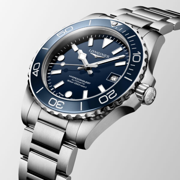Eine Nahaufnahme der Longines HydroConquest mit einem Edelstahlgehäuse, einer blauen Drehlünette, einem blauen Zifferblatt mit silbernen Indexen und einem Datumsfenster vor einem hellen Farbhintergrund.