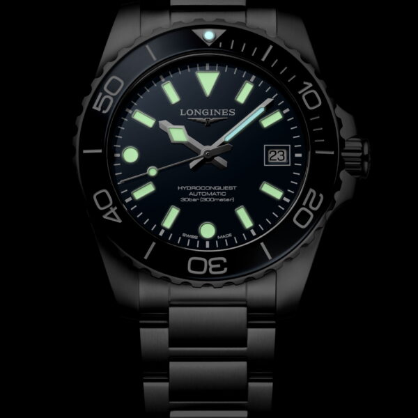 Die Longines HydroConquest ist eine Armbanduhr aus Edelstahl mit einem dunklen Zifferblatt, grün leuchtenden Indexen und Zeigern sowie einem Datumsfenster auf schwarzem Hintergrund.
