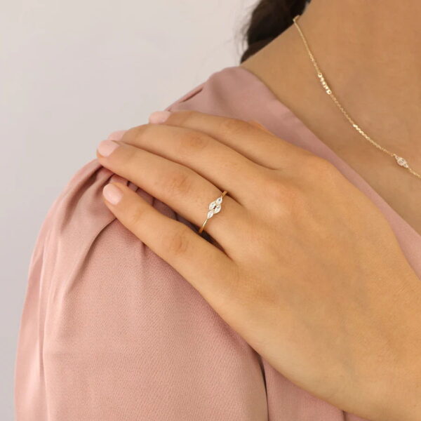 Eine Frauenhand mit manikürten Nägeln ruht auf ihrer Schulter und zeigt den Echtgold-Ring Noélie mit kleinen weißen Steinen. Dazu trägt sie eine passende goldene Halskette und eine hellrosa Bluse.
