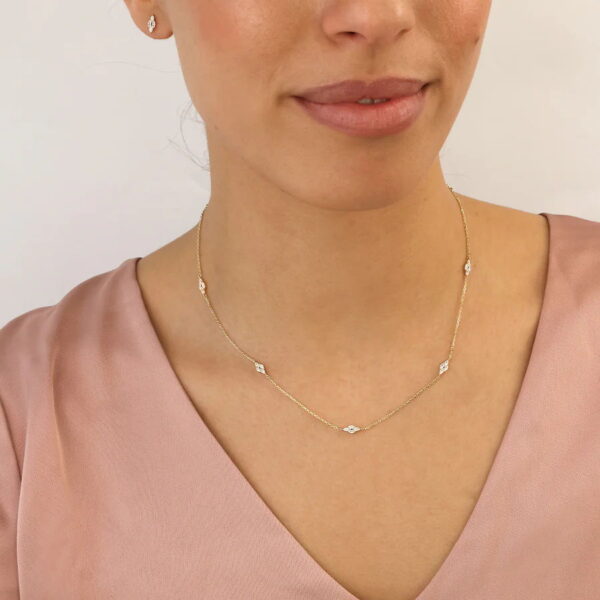 Eine Frau, die ein hellrosa Oberteil mit V-Ausschnitt trägt, präsentiert das Echtgold Collier Noélie, eine zarte Goldkette mit kleinen diamantförmigen Akzenten und passenden Ohrsteckern, vor einem schlichten hellen Hintergrund.