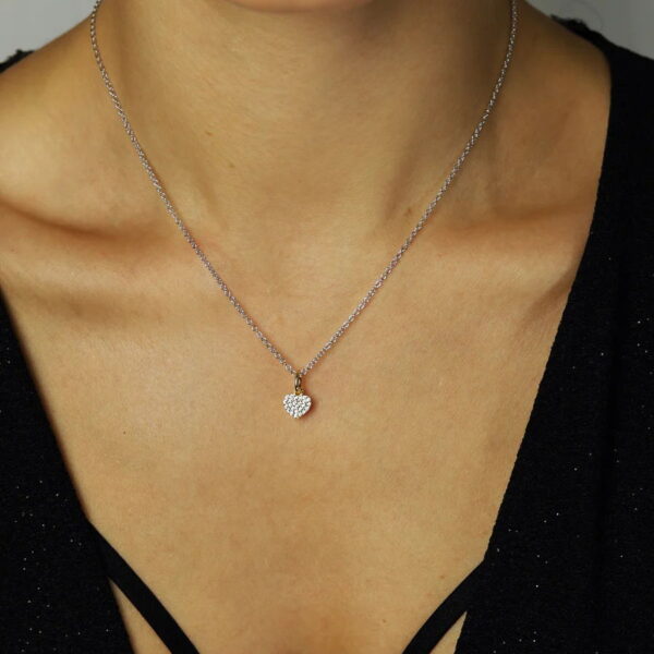 Eine Person trägt die Sweet Glam Halskette Herz, eine zarte Silberkette mit einem kleinen funkelnden Herzanhänger, die über einem schwarzen Oberteil mit V-Ausschnitt liegt.