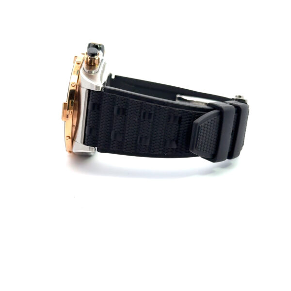 Die Breitling Super Chronomat B01 44 verfügt über ein schwarzes, strukturiertes Armband und ein Metallgehäuse, das sich seitlich vor einem weißen Hintergrund abzeichnet, wobei das Zifferblatt nicht sichtbar ist.